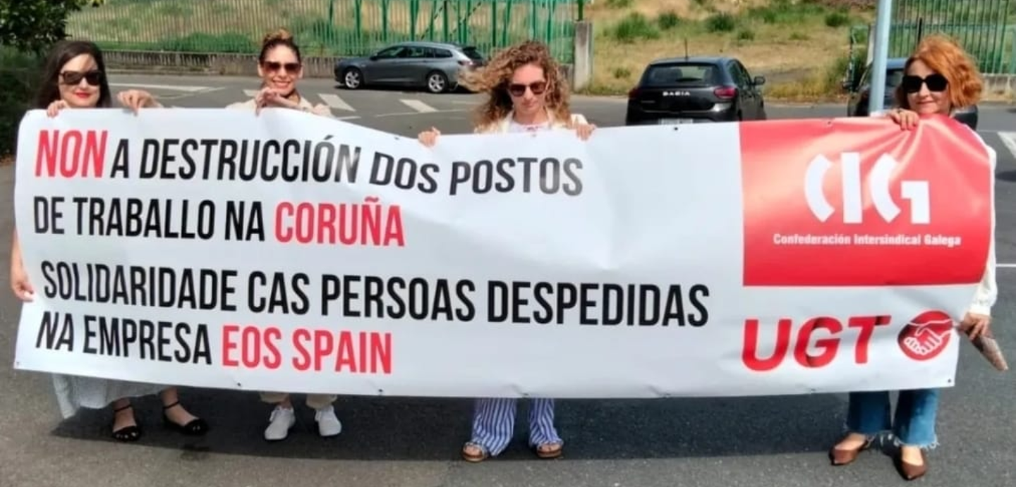 Imaxe dunha concentración previa. Na imaxe están 4 mulleres portando unha pancarta con lema: "Non a destrución dos postos de traballo na Coruña. Solidade cas persoas despedidas na empresa Eos Spain."