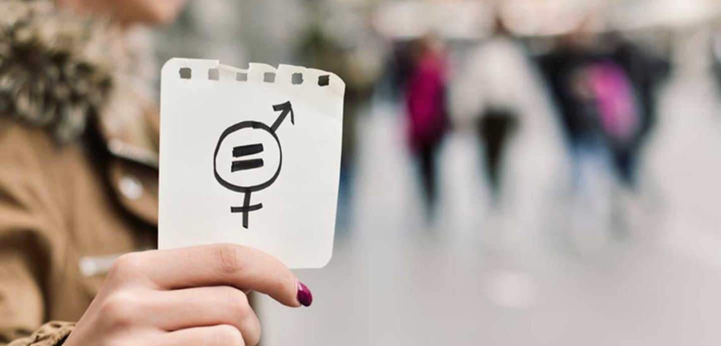Man dunha muller cun papel onde hay debuxado o símbolo masculino e feminino e un igual, simbolizando a igualdade de xénero