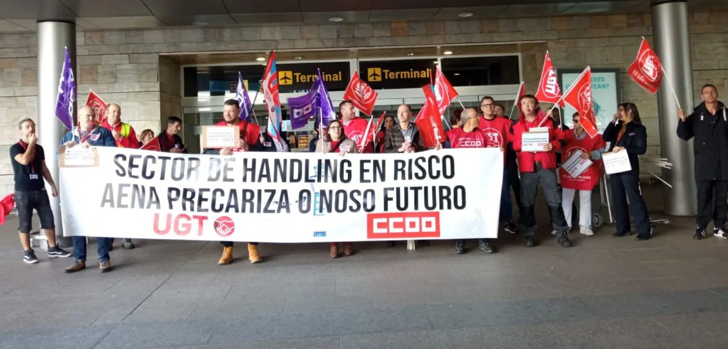 Imaxe da concentración do persoal do handling no aeroporto da Coruña. No cartaz indica " Sector do Handling en risco, Aena precariza o noso futuro". 